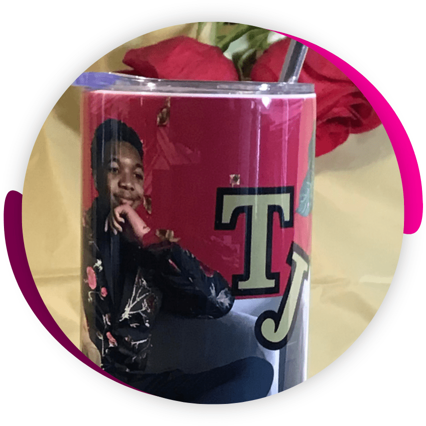 A personalized tumbler with a photo of a person and a letter "t" on a pink background, placed in front of a red rose.