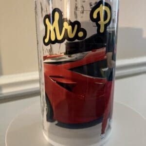 A clear drinking glass with the text "mr. p" and the image of a red sports car on it.