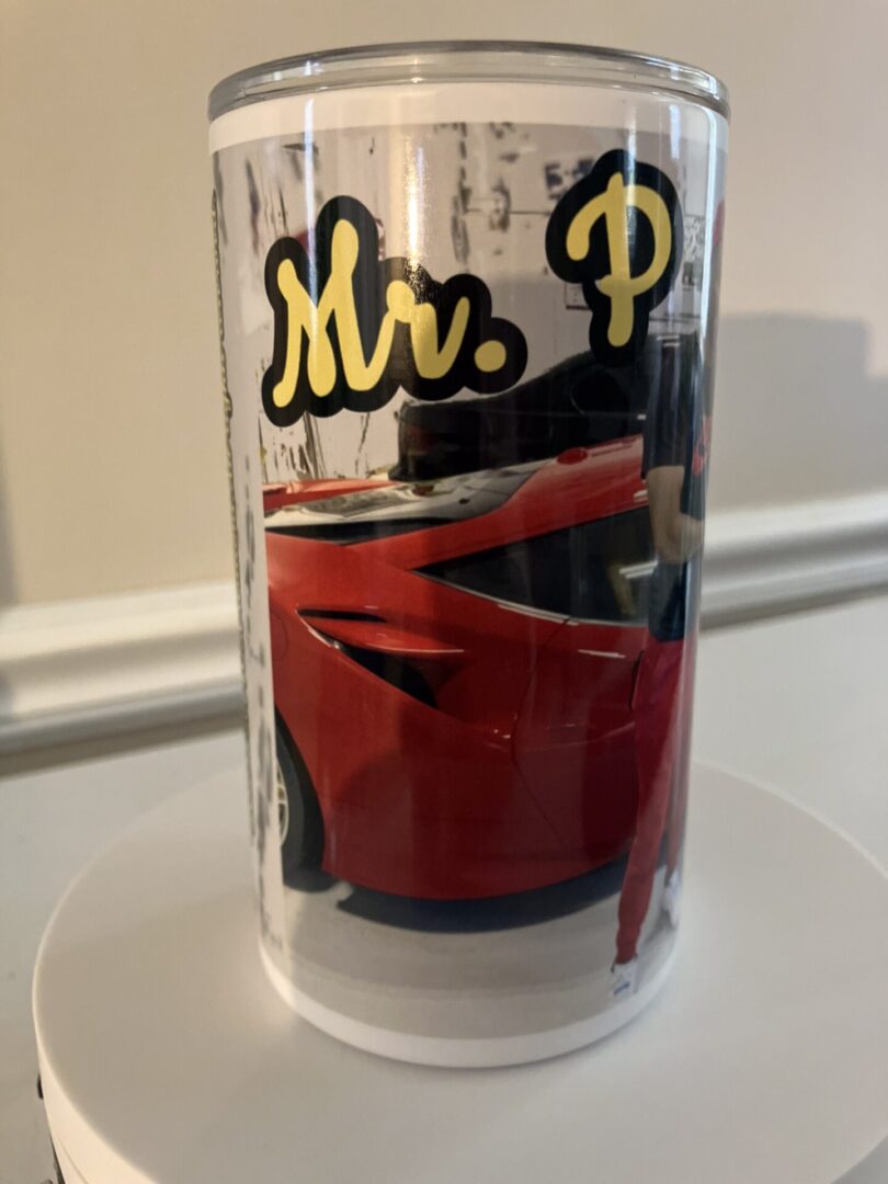 A clear drinking glass with the text "mr. p" and the image of a red sports car on it.