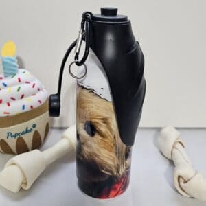 A 20 oz. Pet Water Bottle with an image of a dog on it, flanked by a plush cupcake toy and two rawhide bones.